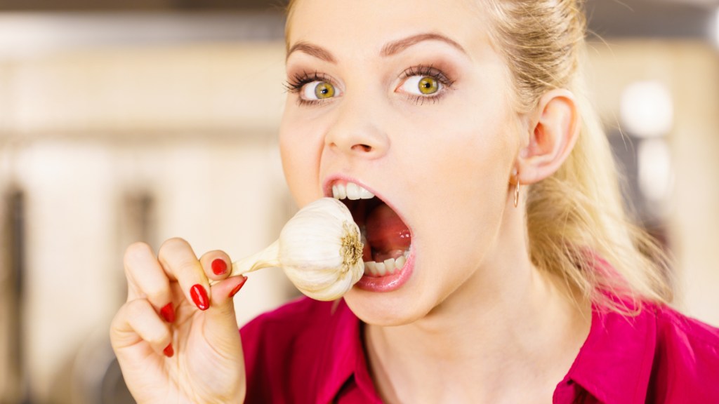 Eine blonde Frau beißt in eine Knoblauch-Knolle.