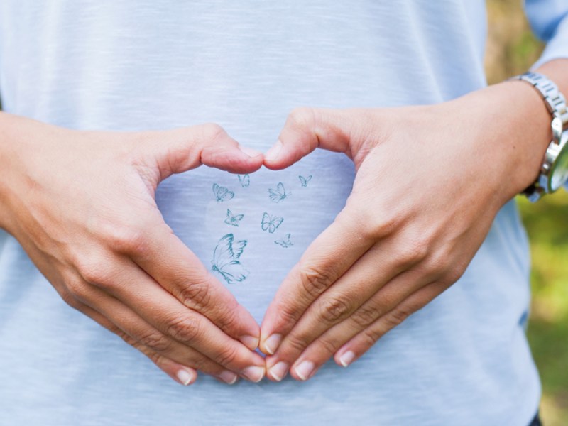 Eine Frau formt vor ihrem Bauch ein Herz mit ihren Händen.