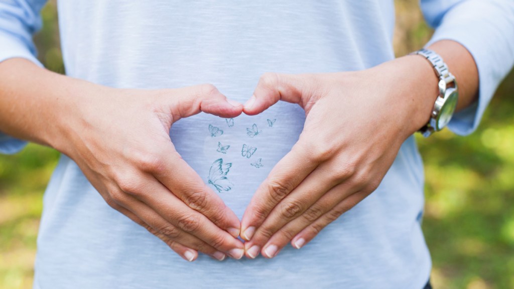 Eine Frau formt vor ihrem Bauch ein Herz mit ihren Händen.