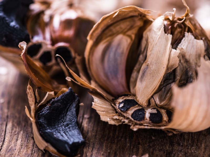 Eine Knolle schwarzer Knoblauch liegt auf einem Holzbrett.