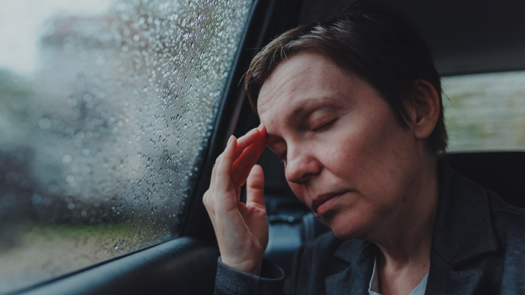 Eine Frau lehnt ihren Kopf an die Scheibe eines Autos und fasst sich mit einer Hand an den Kopf.