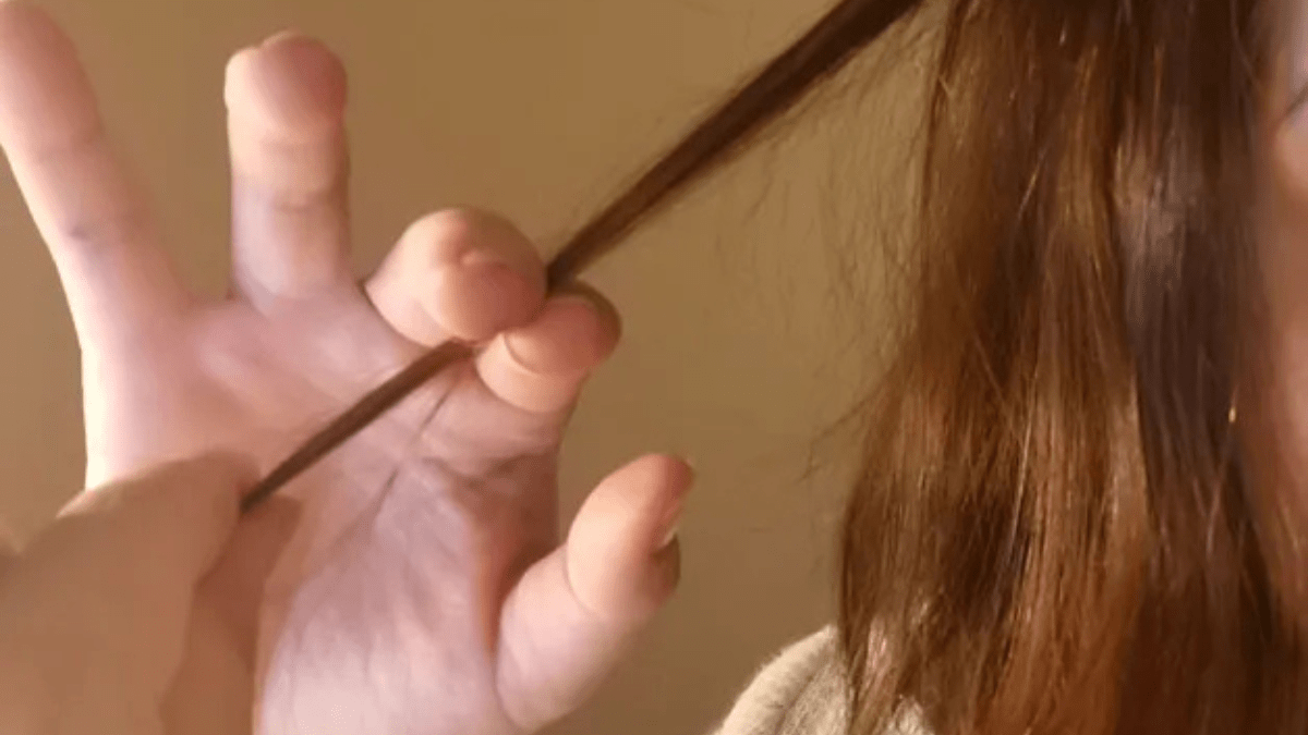 Eine Person mit braunen Haare hÃ¤lt eine HaarstrÃ¤hne in die Kamera.