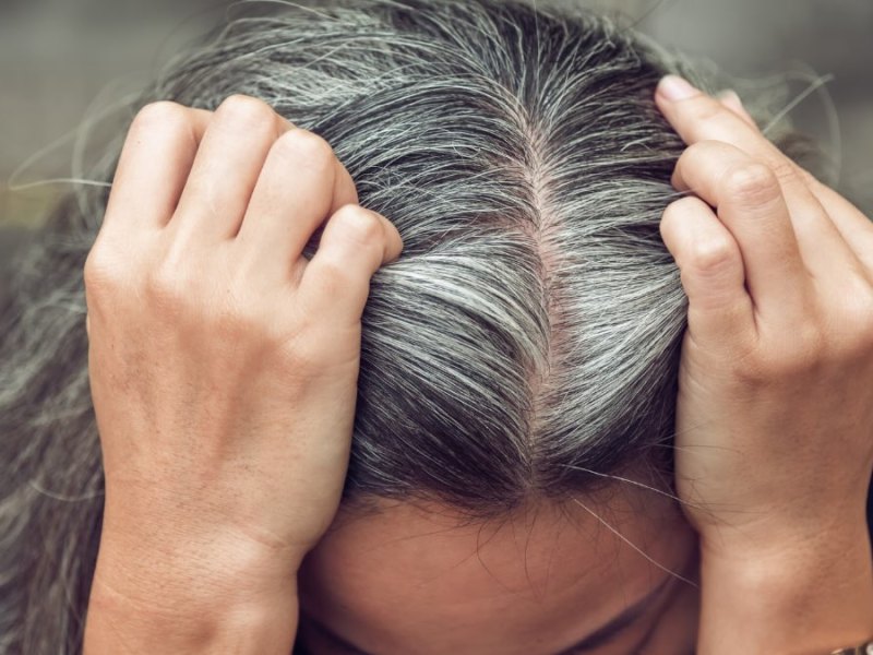 Eine Frau teilt ihren Scheitel und zeigt ihre grauen Haare.