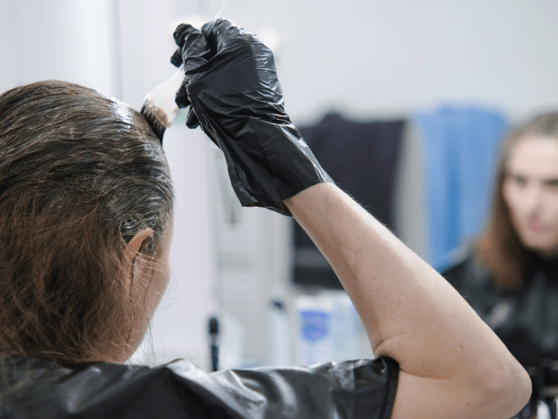 Eine Frau steht vor einem Spiegel und trägt Haarfarbe mit einem Pinsel auf.