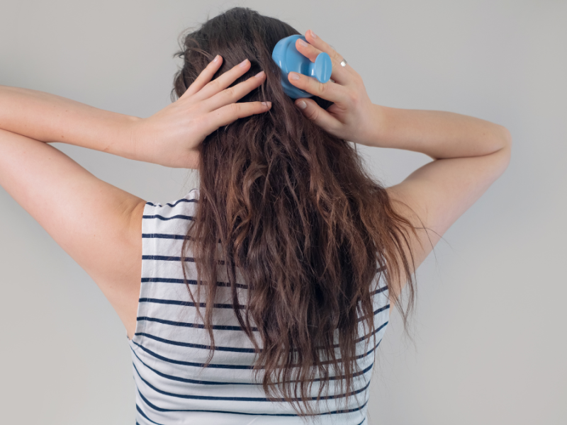 Eine Frau von hinten fotografiert, bürstet ihre langen blonden Haare.