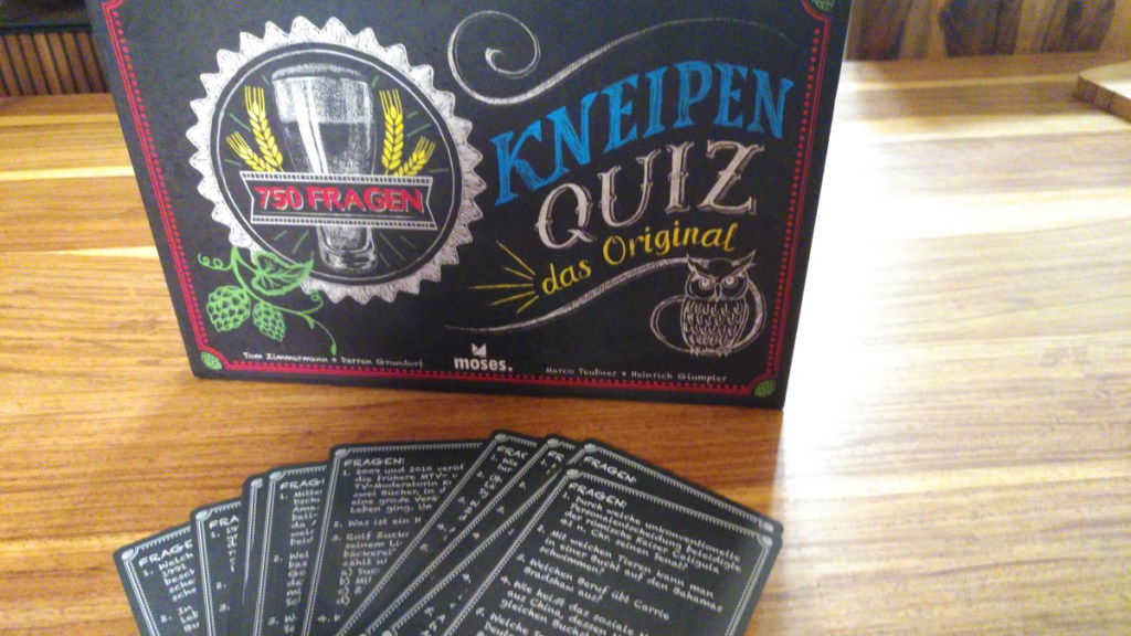 Das Spiel „Kneipenquiz“ steht auf dem Tisch und davor liegen ein paar der Fragenkarten verteilt.