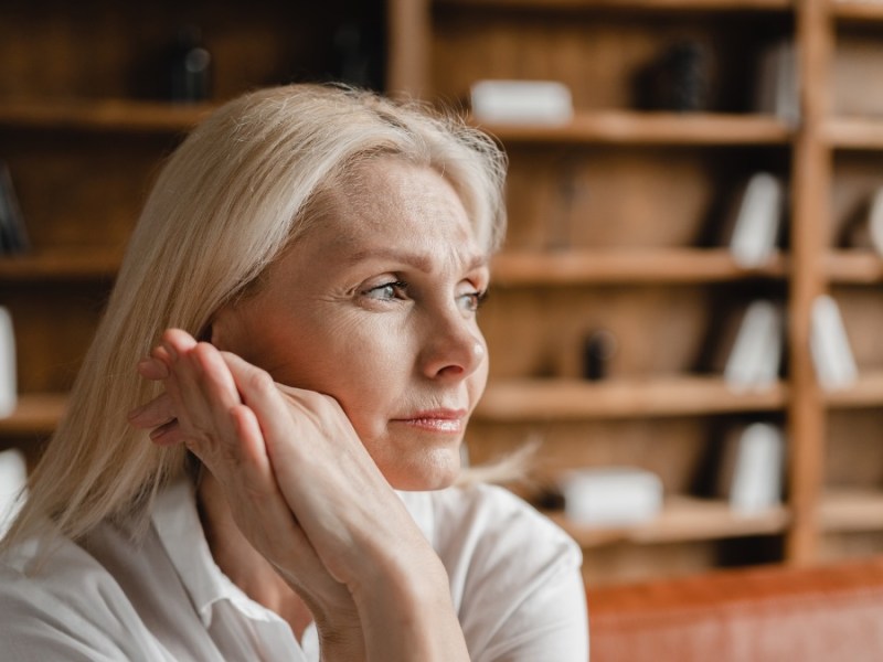 Eine mittelalte Frau mit langen, weiÃŸblonden Haaren schaut nachdenklich in die Ferne.