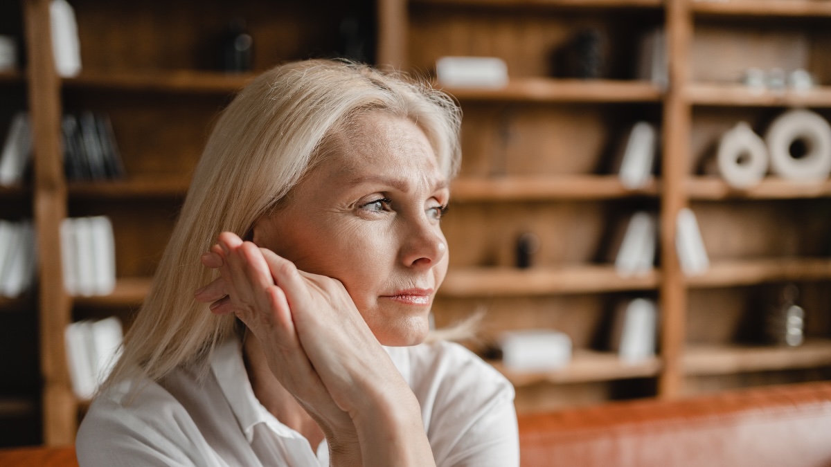 Eine mittelalte Frau mit langen, weißblonden Haaren schaut nachdenklich in die Ferne.