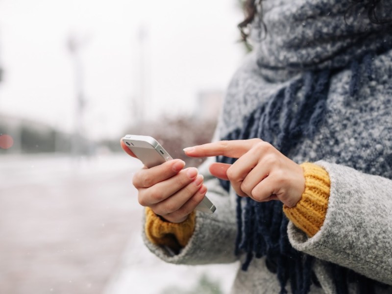 Eine Frau in Winterkleidung tippt auf ihrem Smartphone herum.