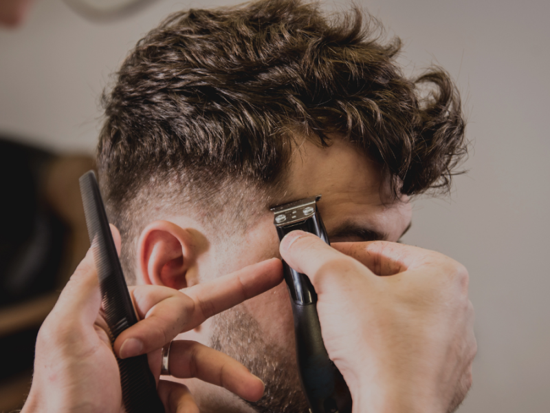 Einem Mann werden die Haare mit einem Rasiere geschnitten.