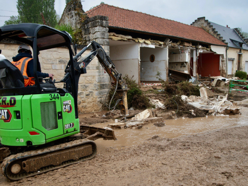 Ein Bagger vor einem zerstörten Haus.