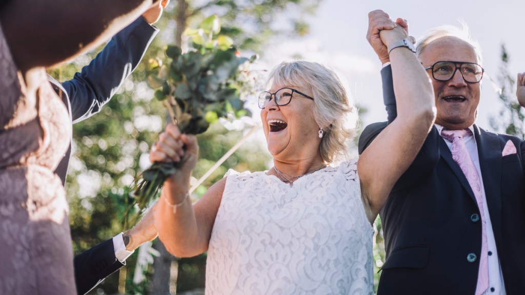 Ein älteres Hochzeitspaar jubelt zusammen mit seinen Gästen.