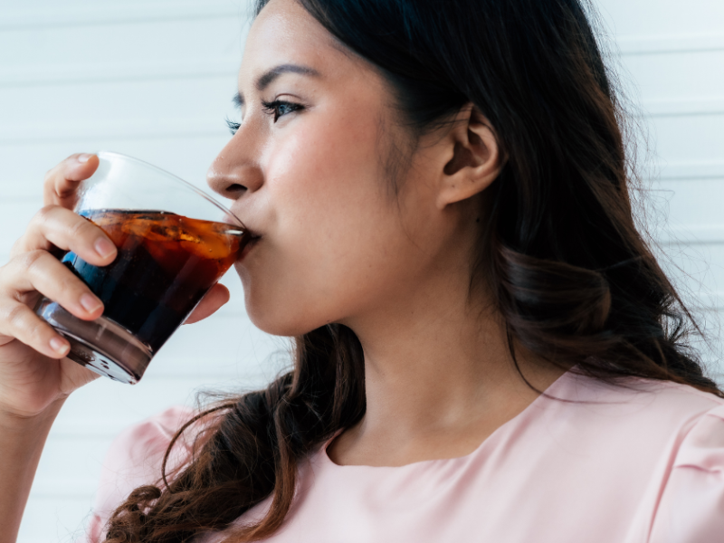 Frau lacht und trinkt ein Glas Cola.