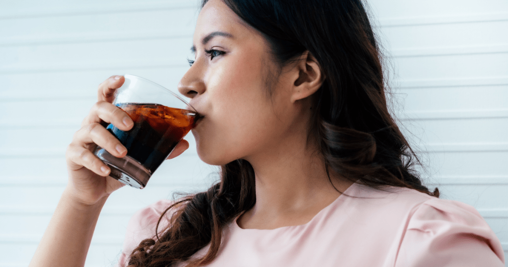 Frau lacht und trinkt ein Glas Cola.
