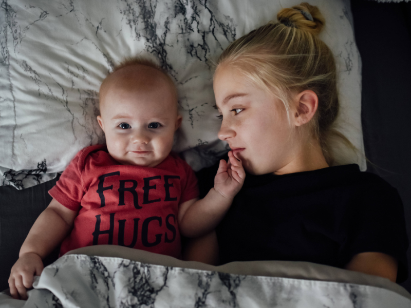 Ein Baby und ein etwas älteres Mädchen liegen gemeinsam im Bett.