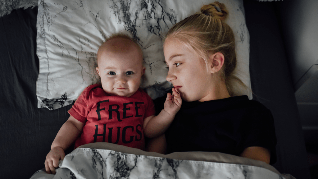 Ein Baby und ein etwas älteres Mädchen liegen gemeinsam im Bett.