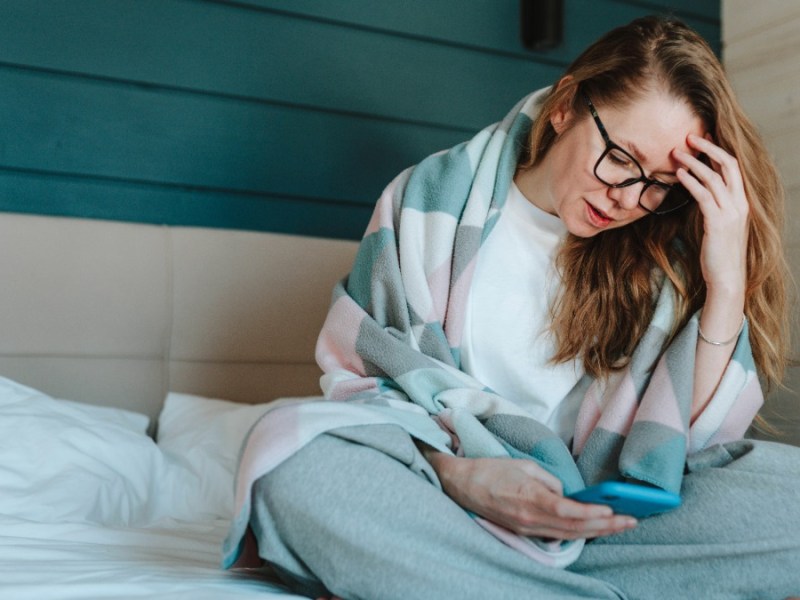 Frau sitzt auf dem Bett und hält ein Handy in der Hand