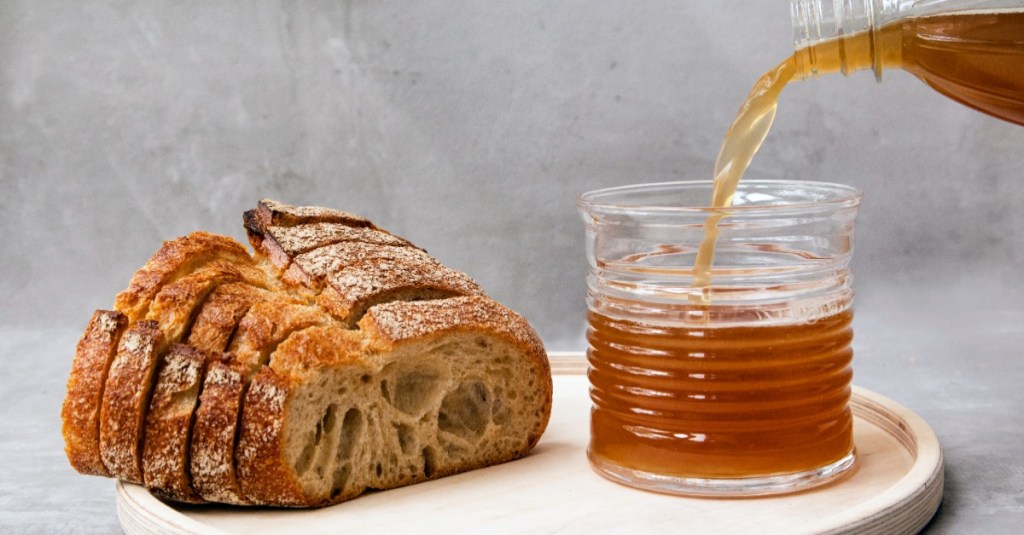 Ein Laib Brot und daneben steht ein Glas, in das eine bräunliche Flüssigkeit gegossen wird.