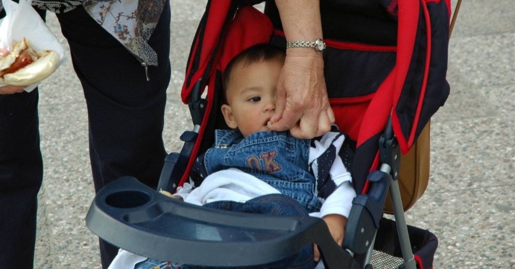 Kind im Kinderwagen wird von Oma mit Brötchen gefüttert