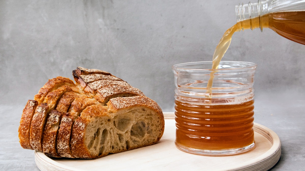 Ein Laib Brot und daneben steht ein Glas, in das eine bräunliche Flüssigkeit gegossen wird.