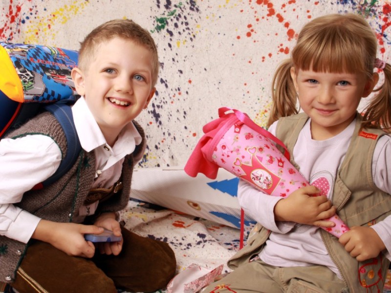 ein Junge mit Schulranzen und ein kleines Mädchen mit einer Zuckertüte sitzen auf dem Boden