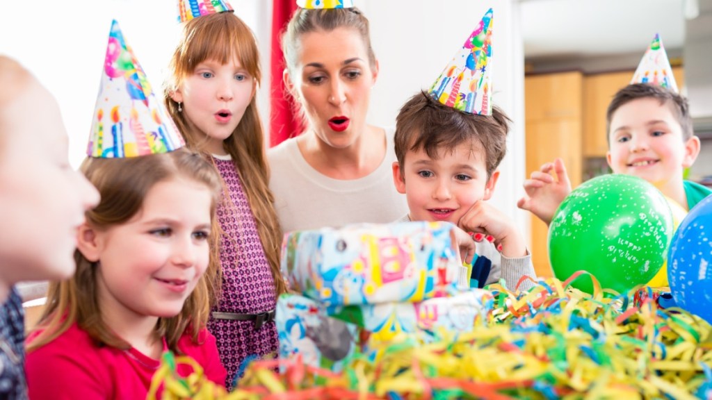 Kleine Kinder mit Partyhüten sitzen an einem Geburtstagstisch