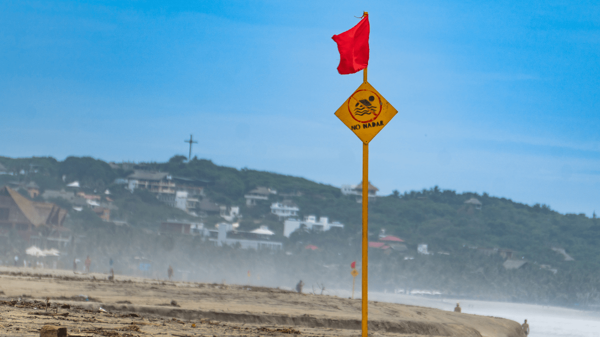 Ein Strand mit einem Schild und einer roten Flagge.