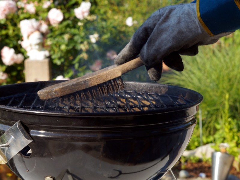 Eine Person reinigt einen Grill mit einer Bürste.