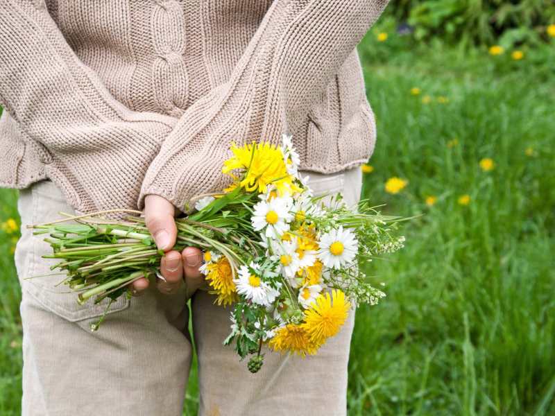 Eine Frau hält einen großen Wildblumenstrauß hinter ihrem Rücken versteckt.