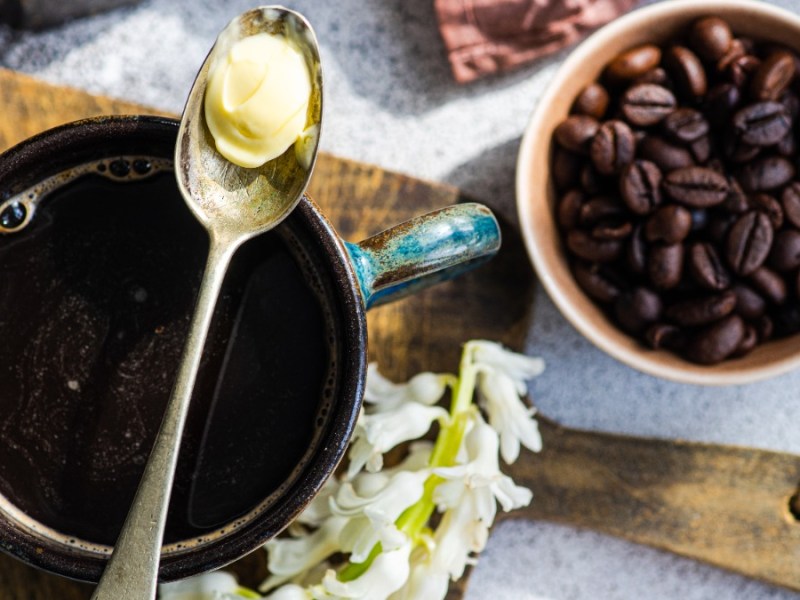 Auf einer Tasse Kaffee liegt ein LÃ¶ffel mit etwas Butter