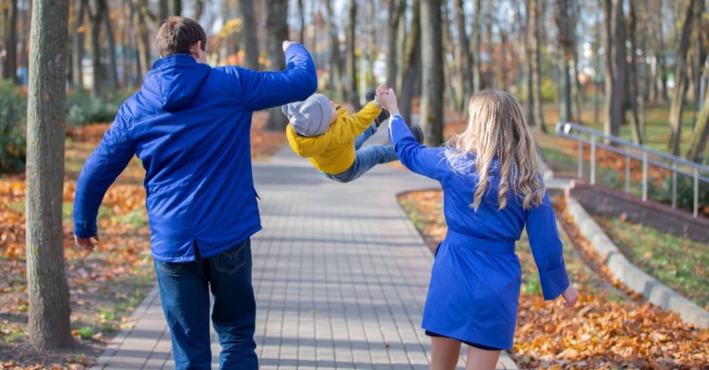 Vater und Mutter schwingen ihren Sohn an den Händen in die Luft