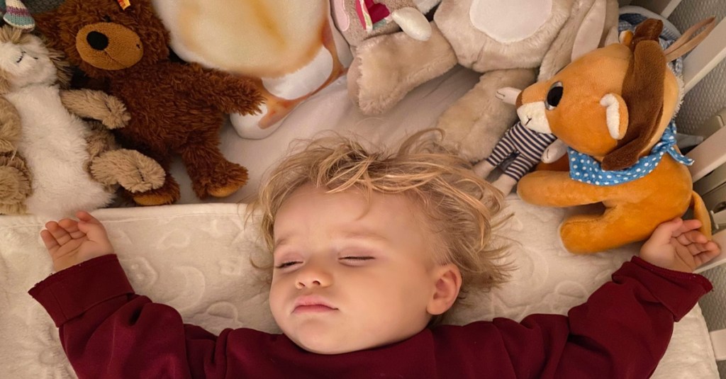 Kleines Kind liegt zufrieden mit seinen Kuscheltieren im Bett.