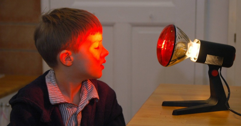 Ein Kind behandelt sein Gerstenkorn mit einer Rotlichtlampe