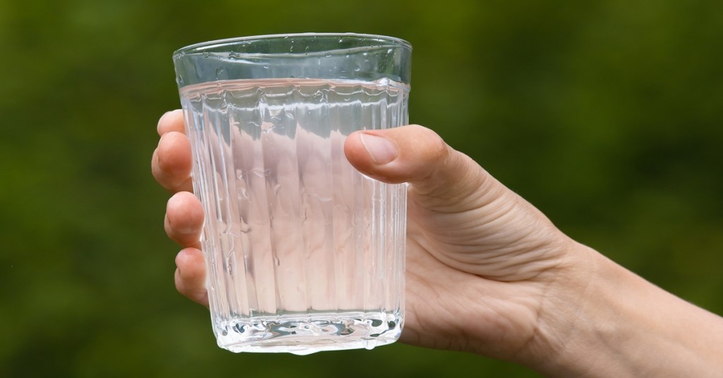 Hand hält Glas mit trübem Wasser