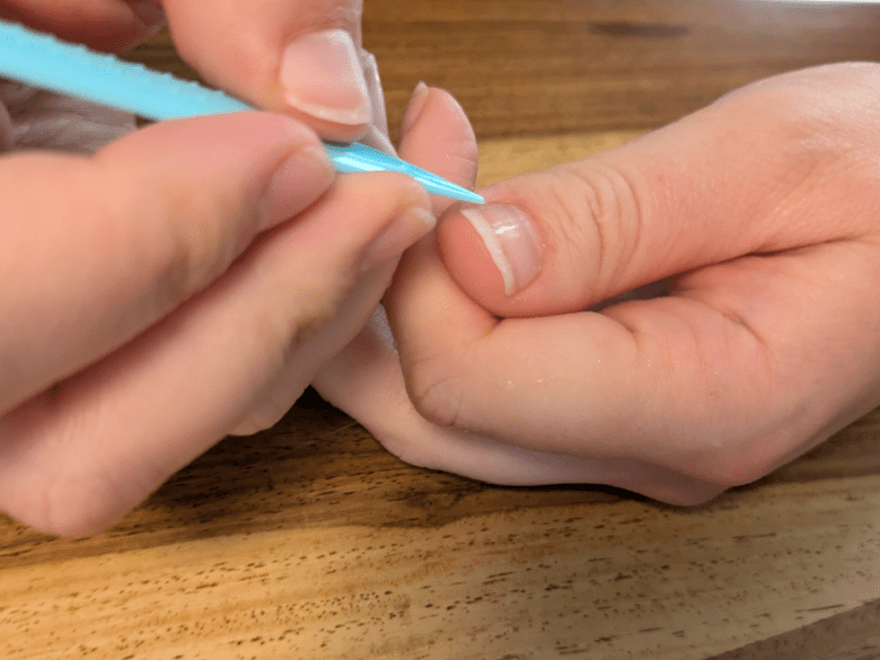 Eine Person schiebt ihre Nagelhaut mit einem Stäbchen zurück.