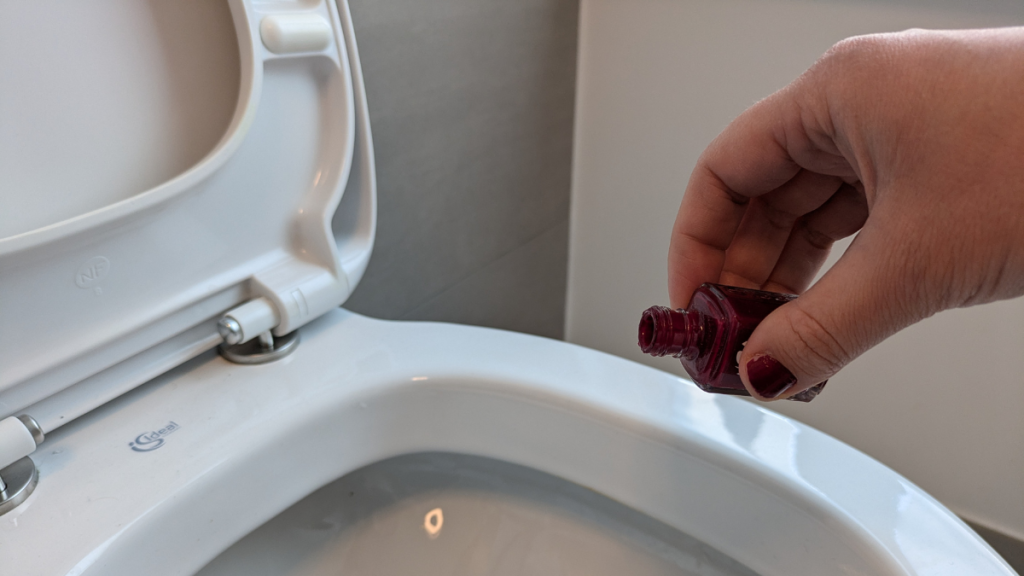 Eine Person schüttet roten Nagellack in die Toilette. 