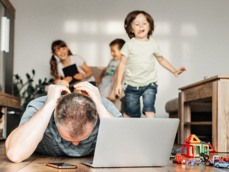 Vater versucht zu Hause am Laptop zu arbeiten, wÃ¤hrend seine Kinder im Hintergrund spielen