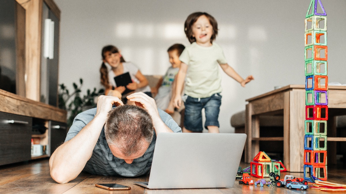 Vater versucht zu Hause am Laptop zu arbeiten, wÃ¤hrend seine Kinder im Hintergrund spielen