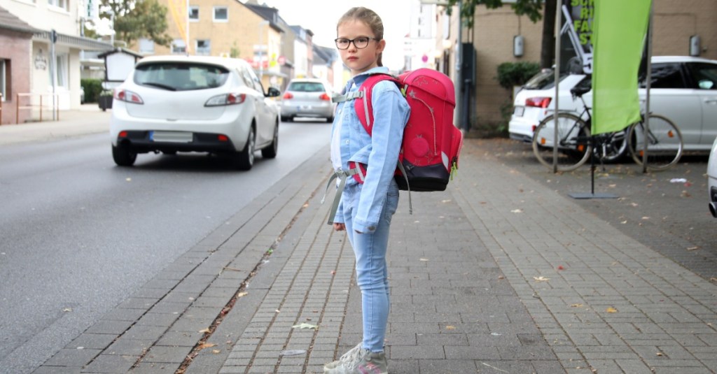 sicherer Schulweg: ein Mädchen möchte eine viel befahrene Straße überqueren