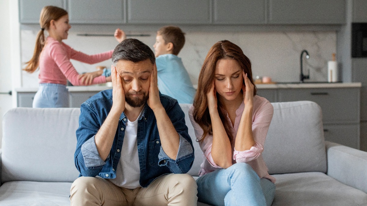 Eltern sitzen genervt auf der Couch, wÃ¤hrend sich die Kinder im Hintergrund streiten