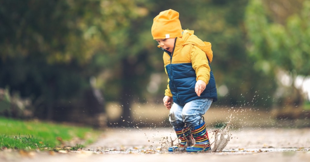 glückliches Kind springt in eine Regenpfütze