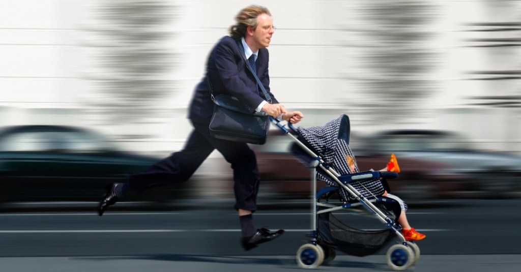 Ein Businessmann rennt mit einem Kinderwagen die Straße entlang