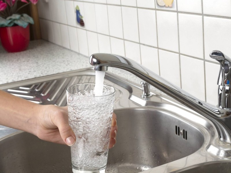 Jemand hÃ¤lt ein Glas unter einen Wasserhahn in der KÃ¼che und fÃ¼llt es mit Wasser.