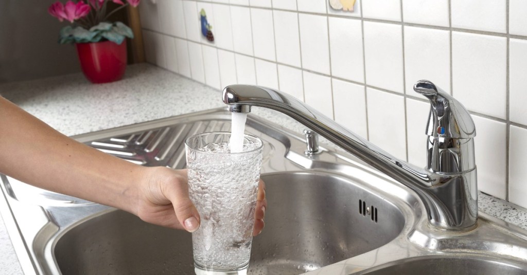 Jemand hält ein Glas unter einen Wasserhahn in der Küche und füllt es mit Wasser.