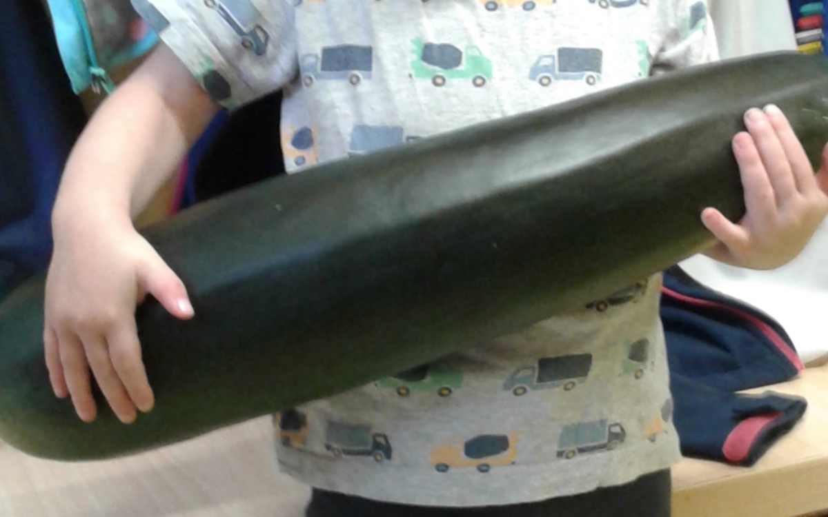 Ein kleines Mädchen hält eine riesige Zucchini im Arm.