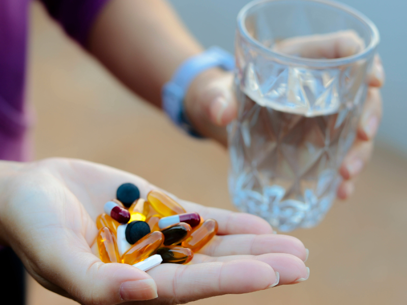 Eine Hand hÃ¤lt viele verschiedene Tabletten, die andere ein Glas Wasser.