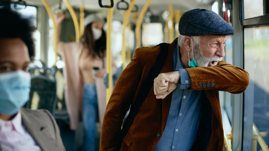 Ein Mann mit heruntergezogener Maske niest in einem Bus.