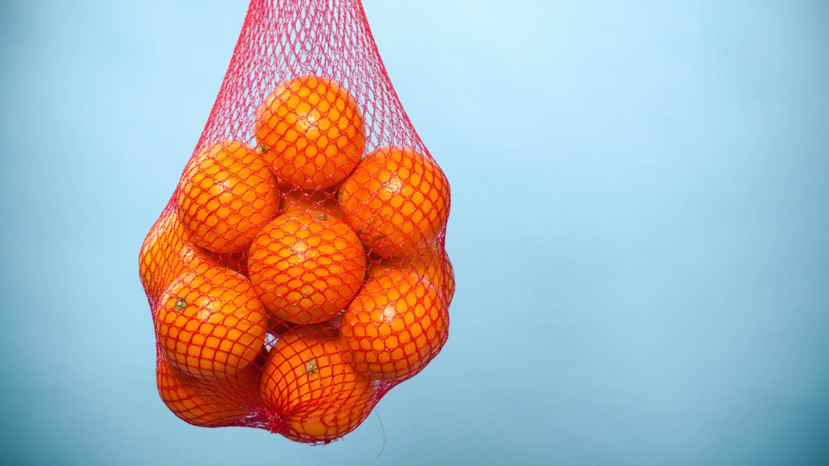 Orangen in einem roten Netz vor einem blauen Hintergrund