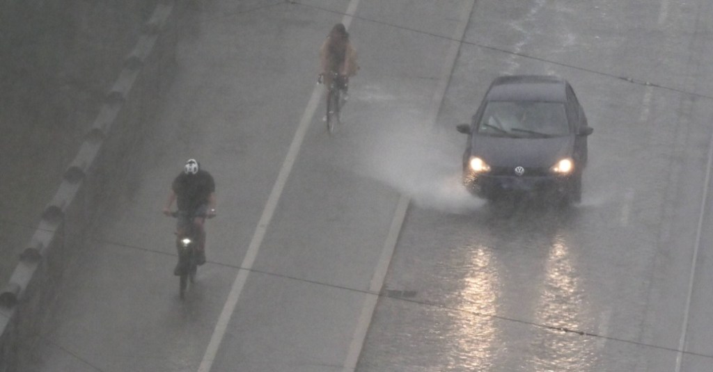 zwei Radfahrer fahren auf dem Radweg, ein Auto auf der Straße fährt durch eine Pfütze