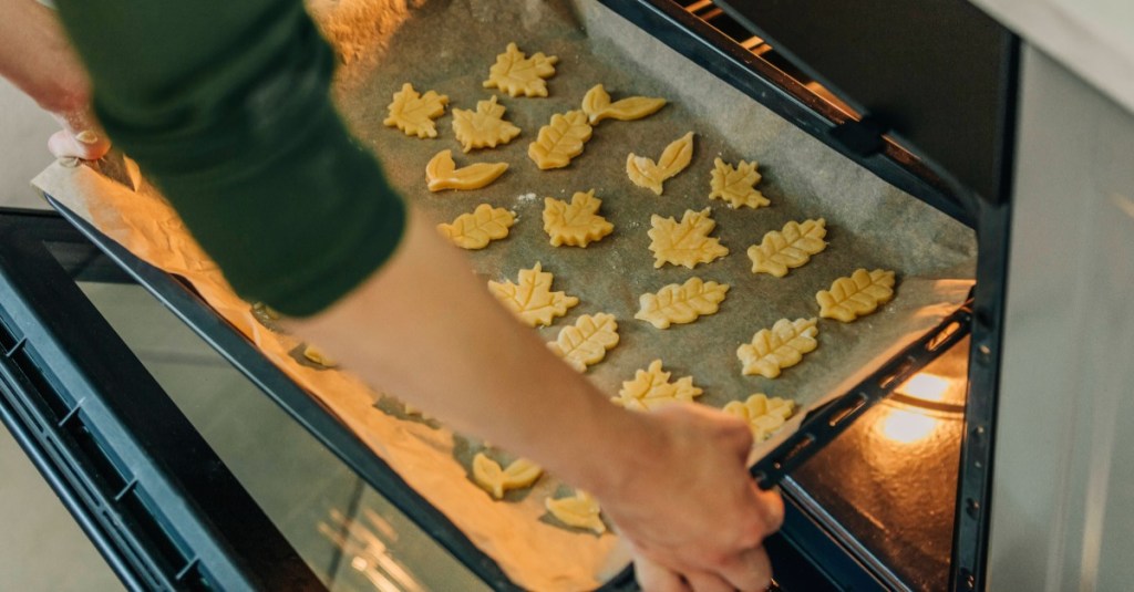 Frau schiebt ein Backblech mit Backpapier und Plätzchen in den Ofen